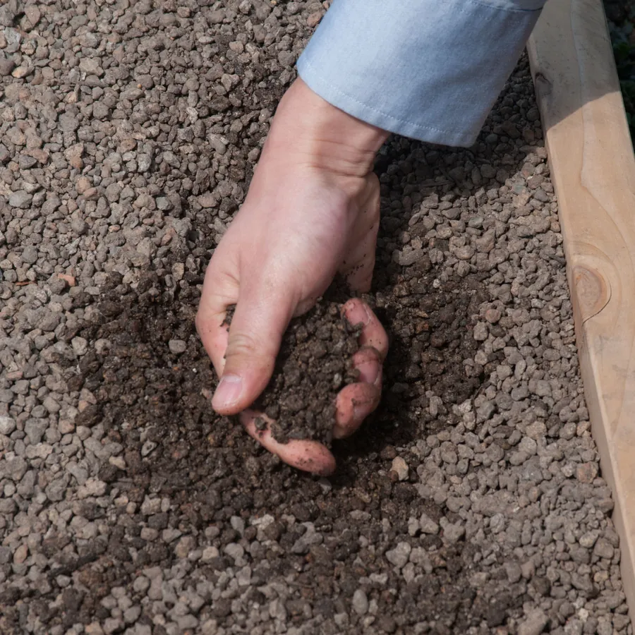A hand lifting a scoop of dark potting mix from a raised bed